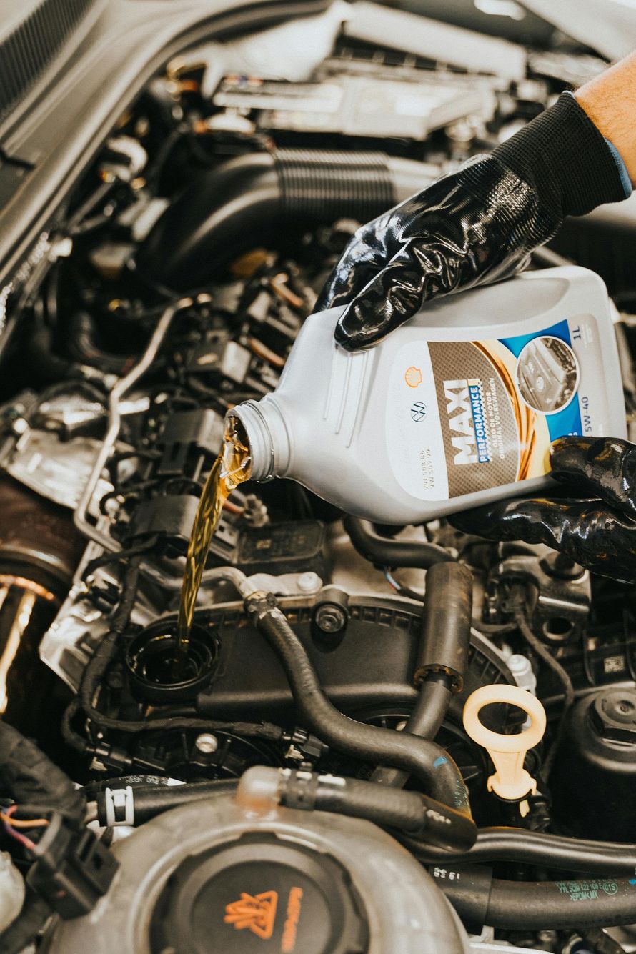 Gloved hand pouring oil into a car engine, filling the compartment with golden liquid.