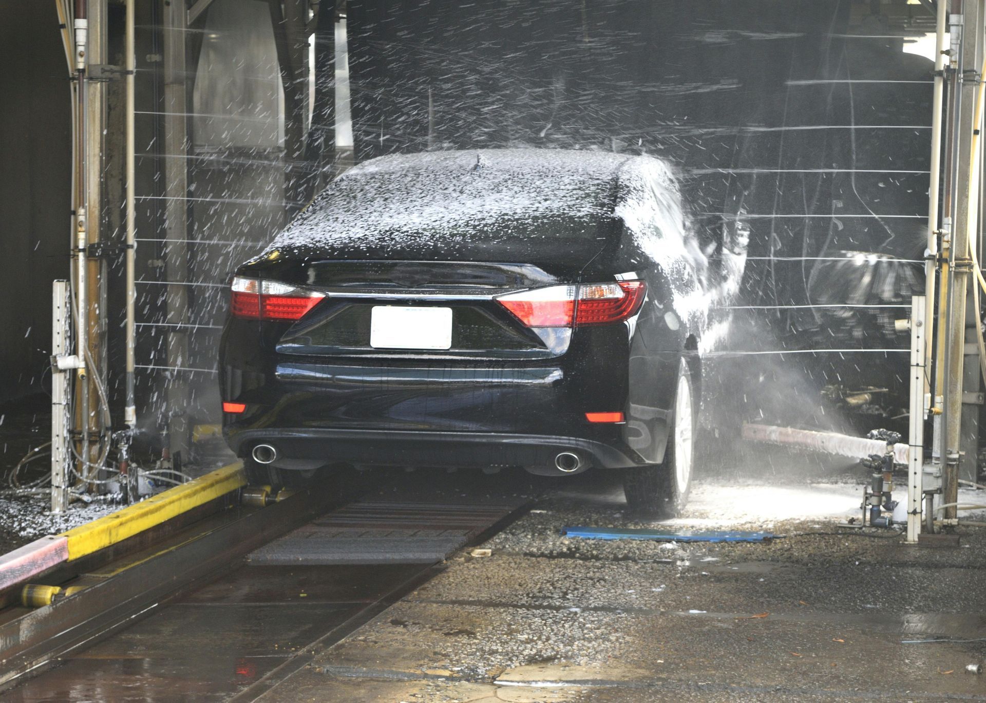 Black car in a car wash, covered in soap suds, being cleaned.