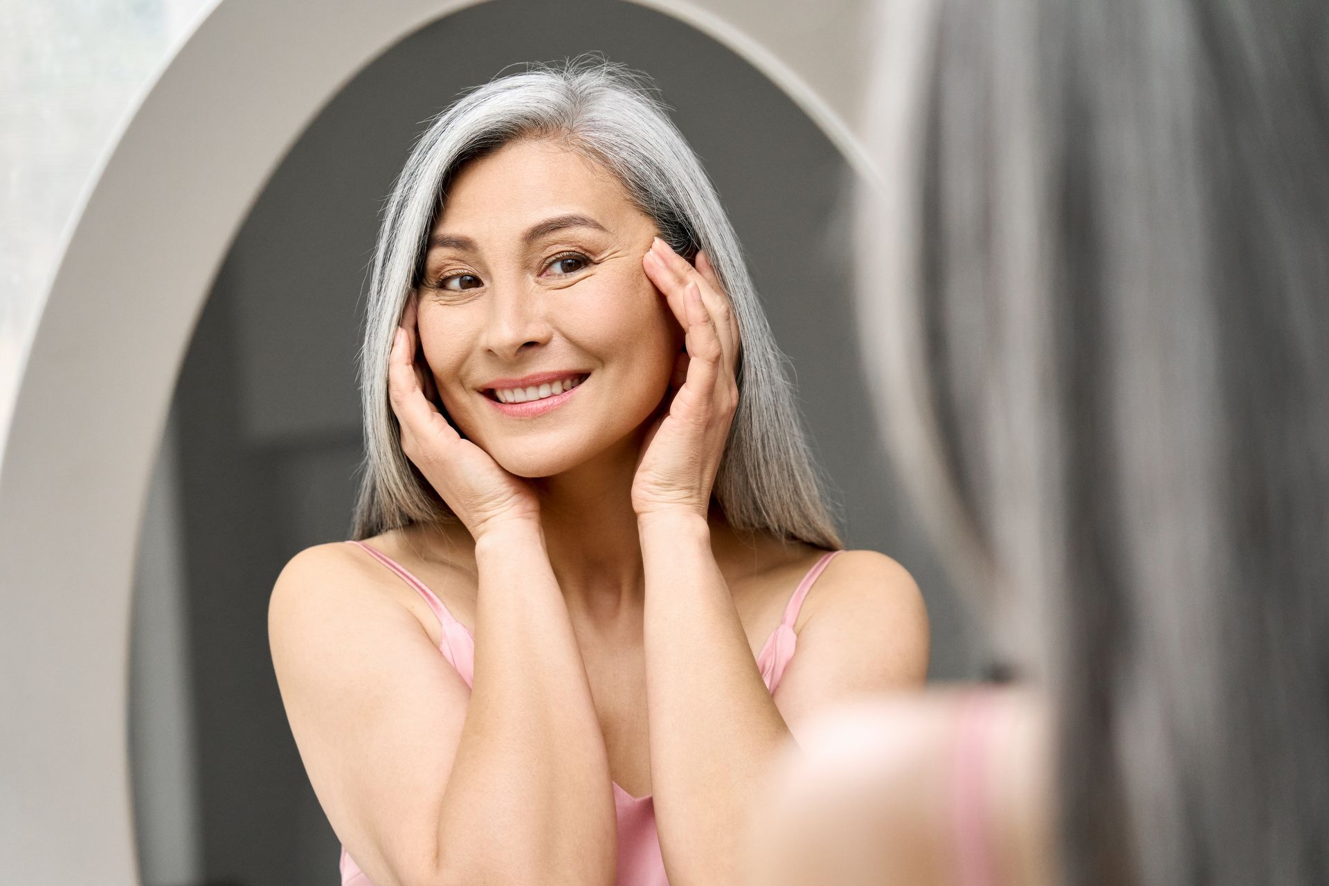 middle aged happy asian woman looking in mirror
