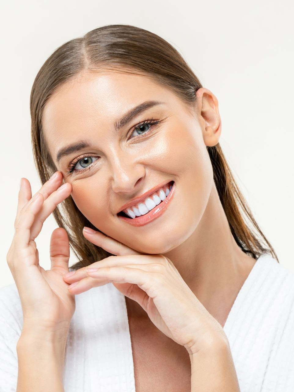 Woman smiling, touching face, glowing skin, hands near face.
