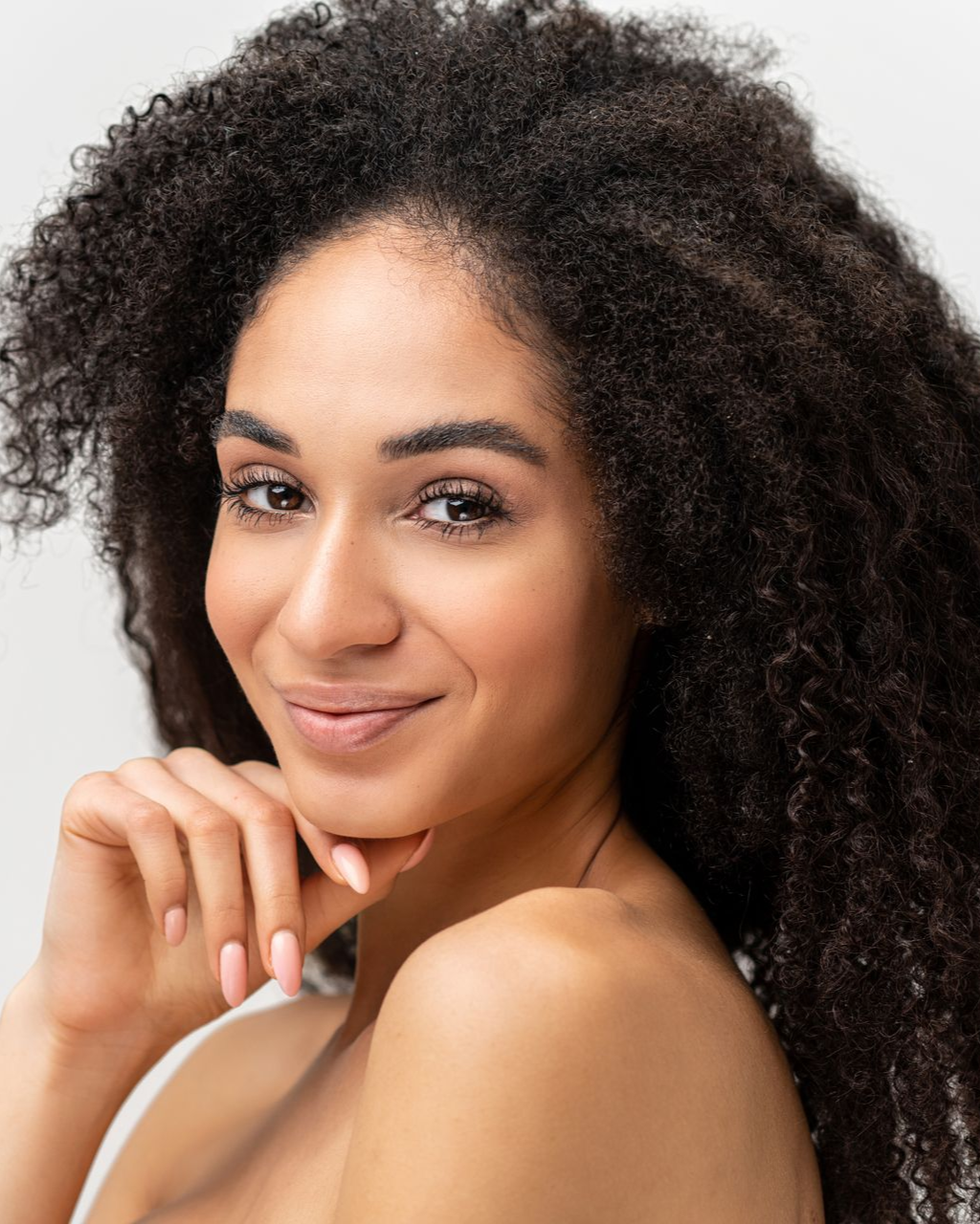 Woman with dark, curly hair smiles, resting chin on hand.