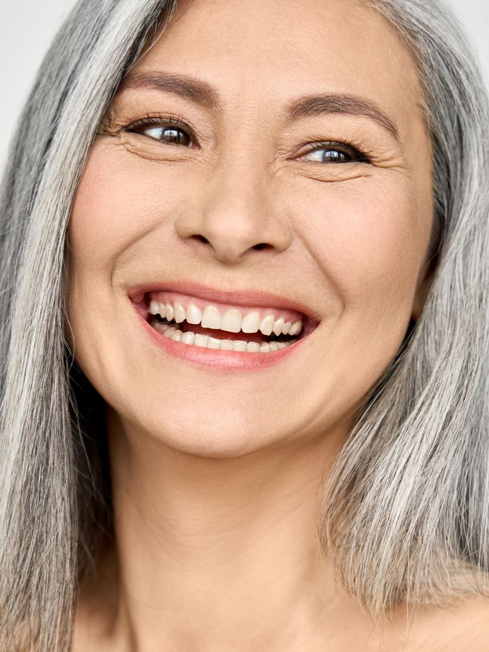 Smiling person with silver hair, looking to the side, teeth visible.