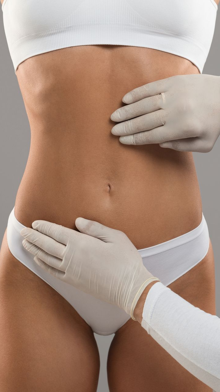 Hands in gloves examining a person's abdomen, wearing white underwear and a crop top.