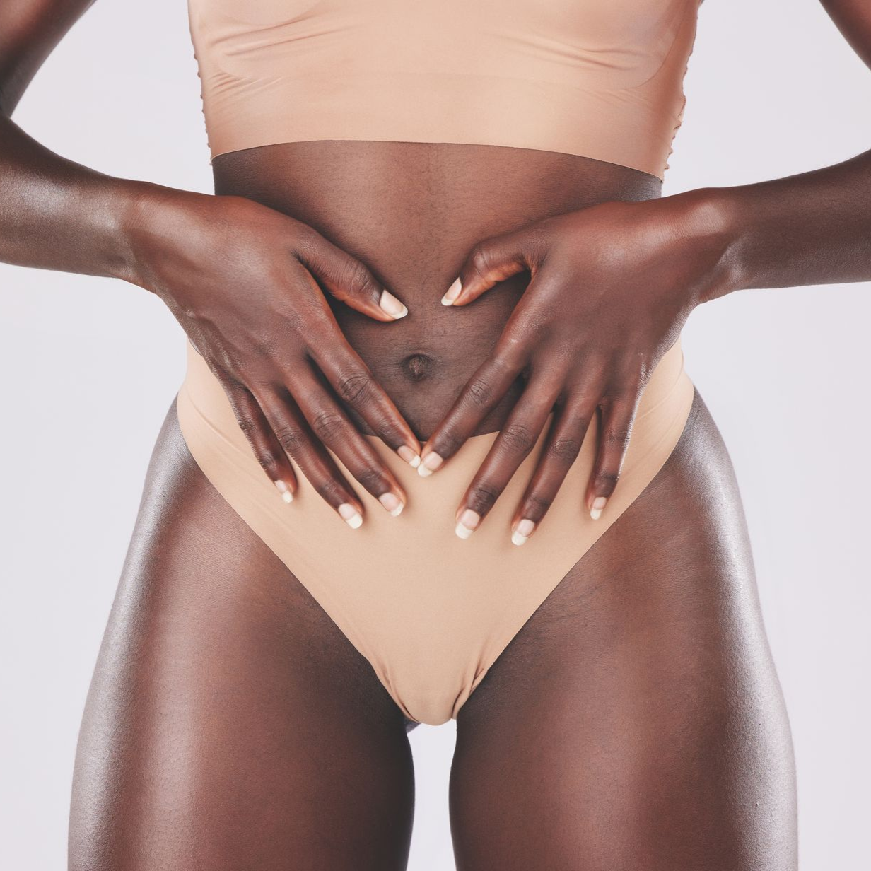 Hands forming a heart shape over a person's abdomen, wearing nude underwear and top.