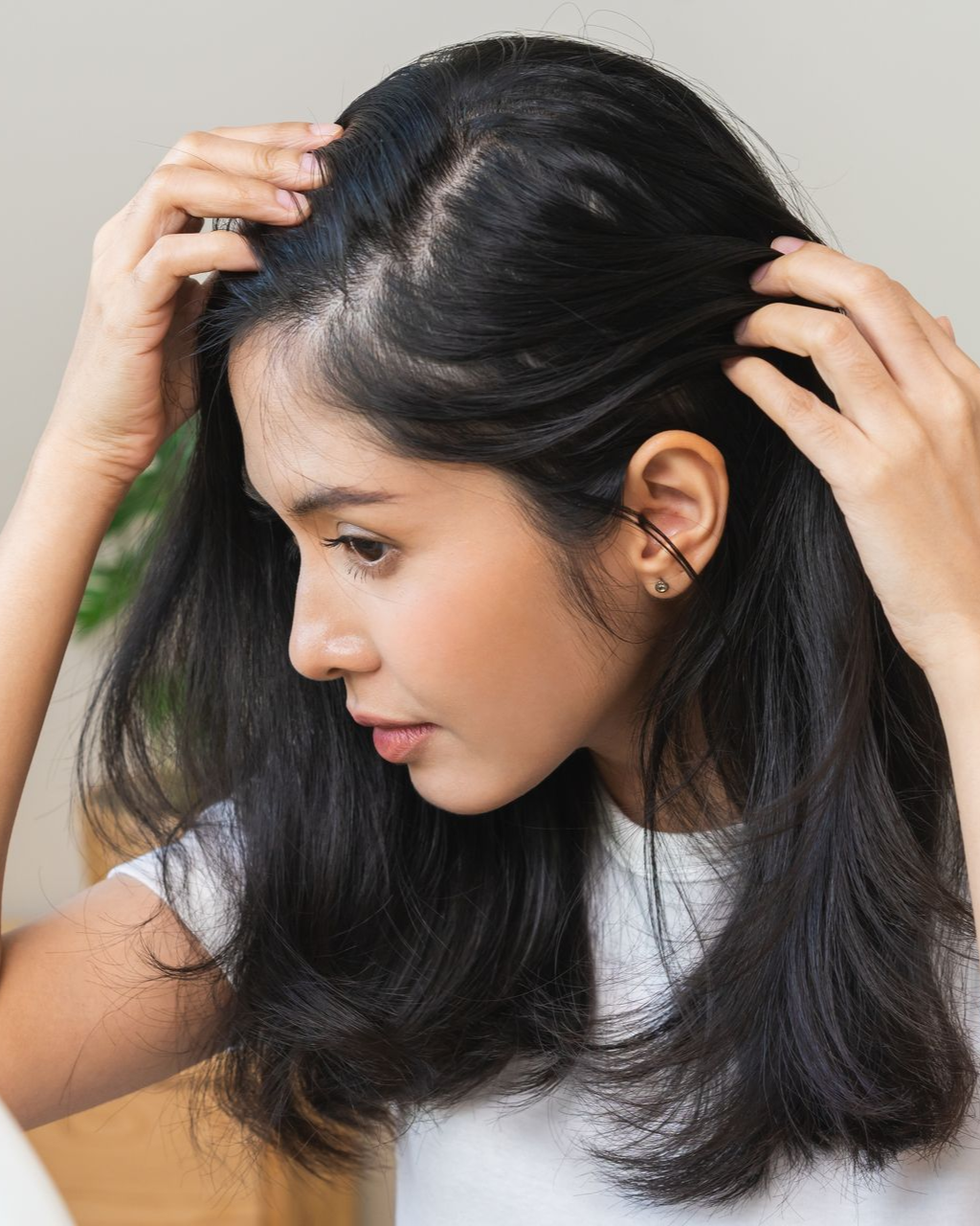 Woman checking hair for thinning; indoors.