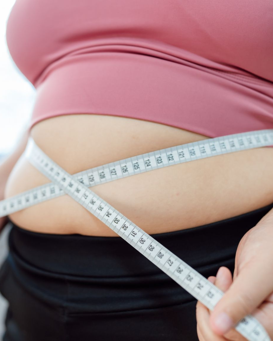 Person measuring their waist with a tape measure, highlighting abdominal area.