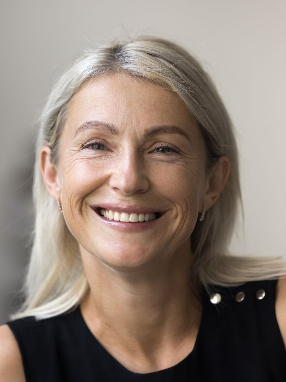 Woman with light blonde hair smiling, wearing a black top.