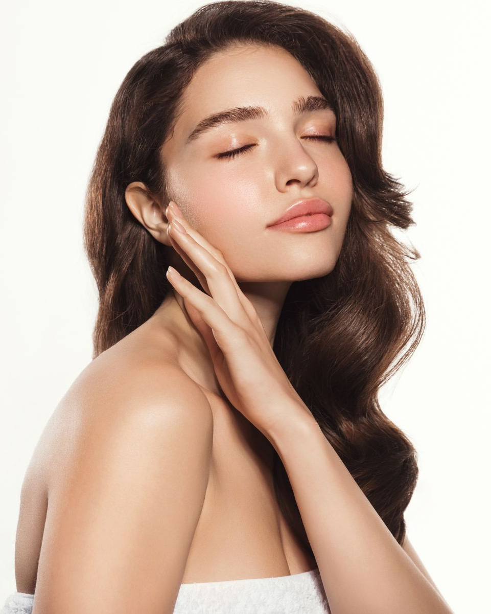 Woman with wavy brown hair, eyes closed, touching her cheek.