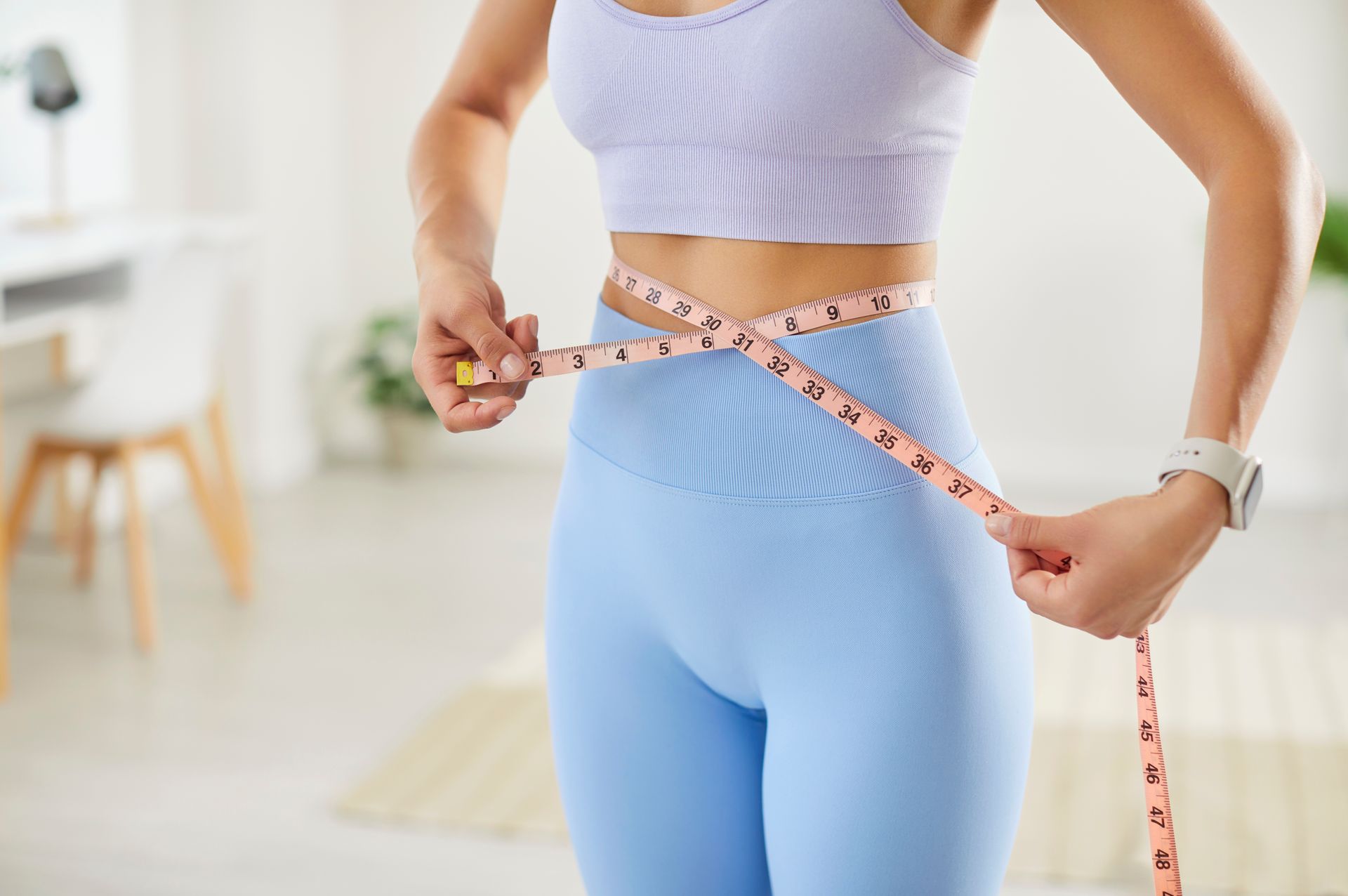 Person in athletic wear measuring their waist with a tape measure.
