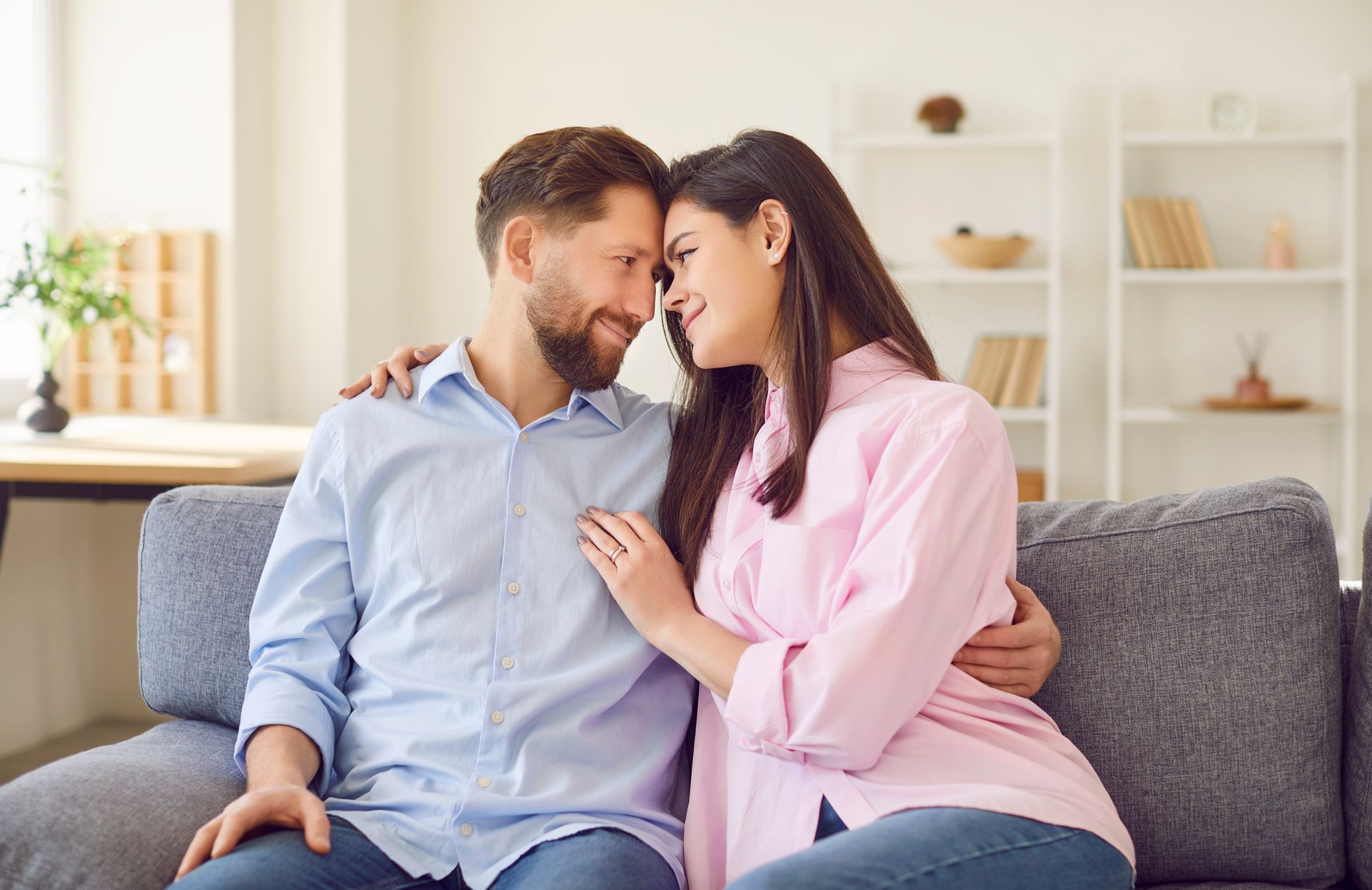 Couple embracing on a couch, smiling and looking at each other, in a living room.
