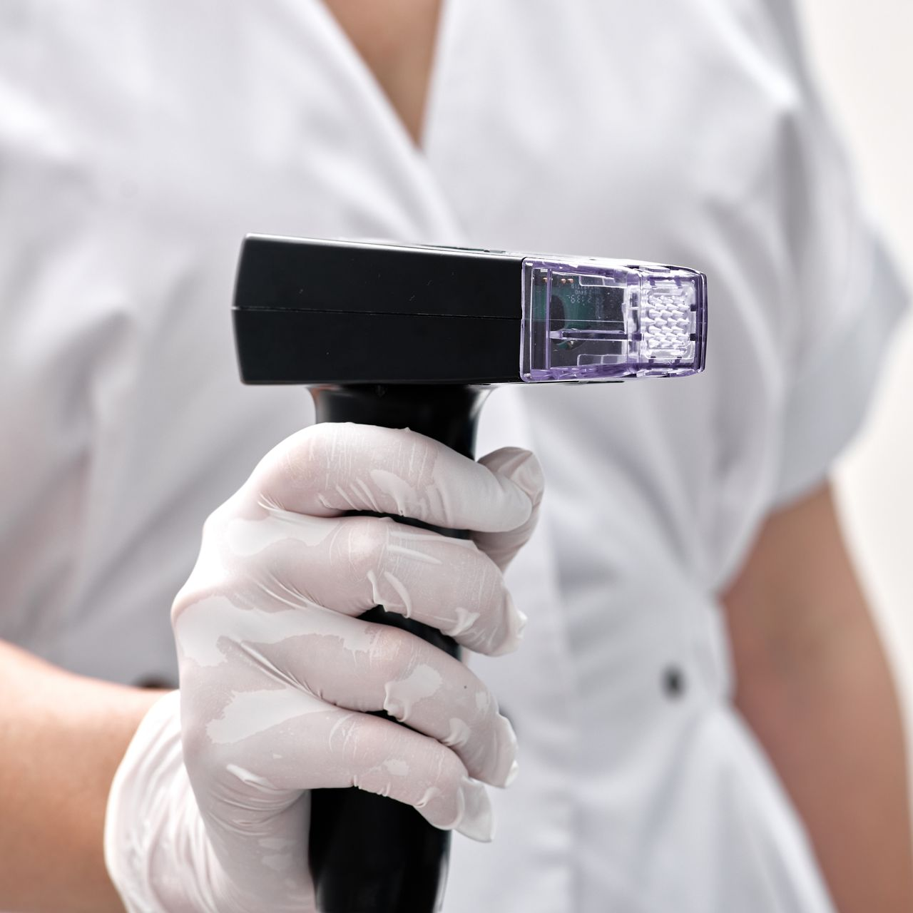 Gloved hand holding a black and clear medical device, possibly for skin treatments.