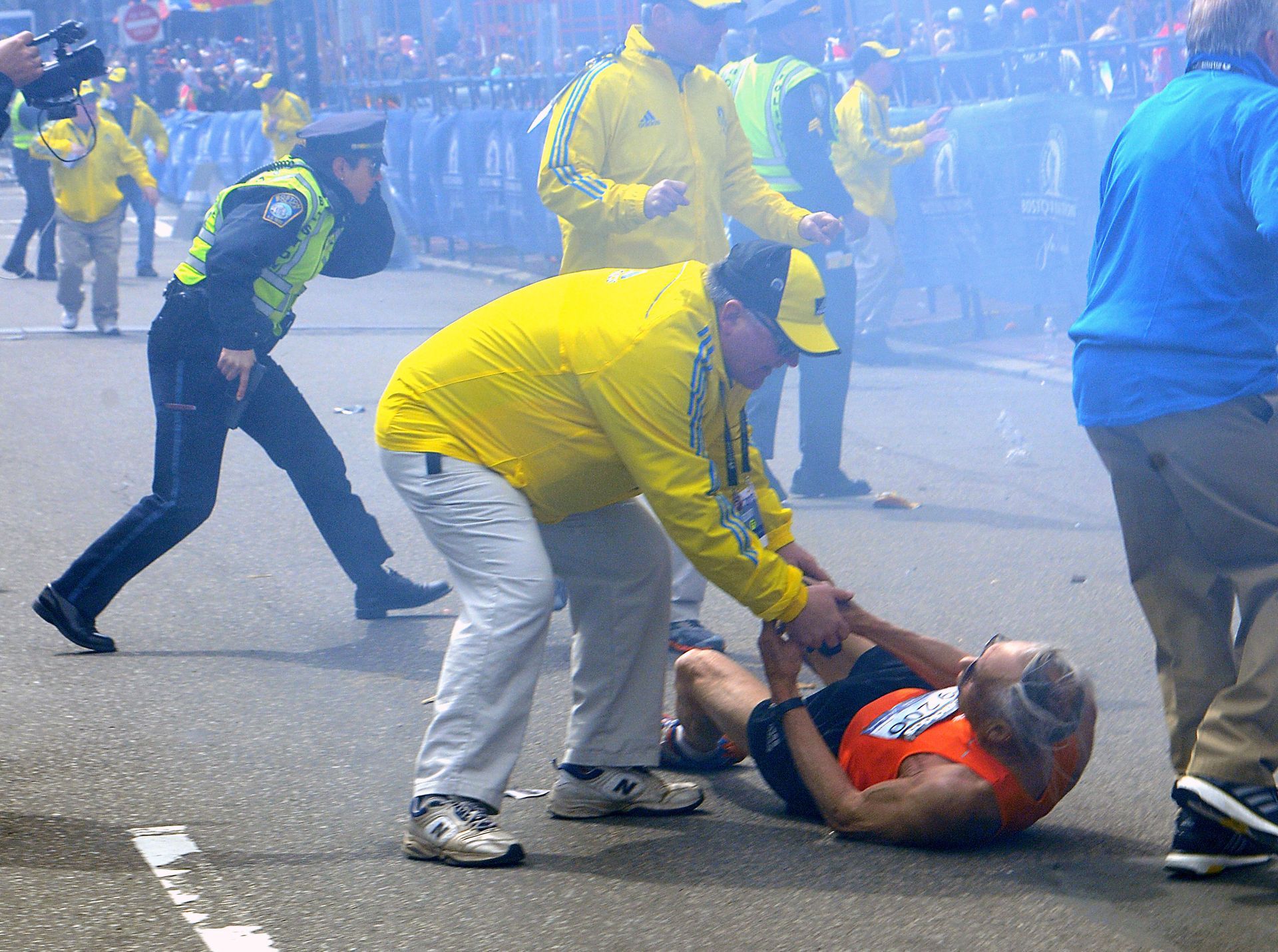 Bill Iffrig, 78, of Lake Stevens, Washington state, is assisted by a race official after collapsing as a Boston Police officer draws her weapon moments after a bombing at the Boston Marathon finish line on Monday, April 15, 2013.