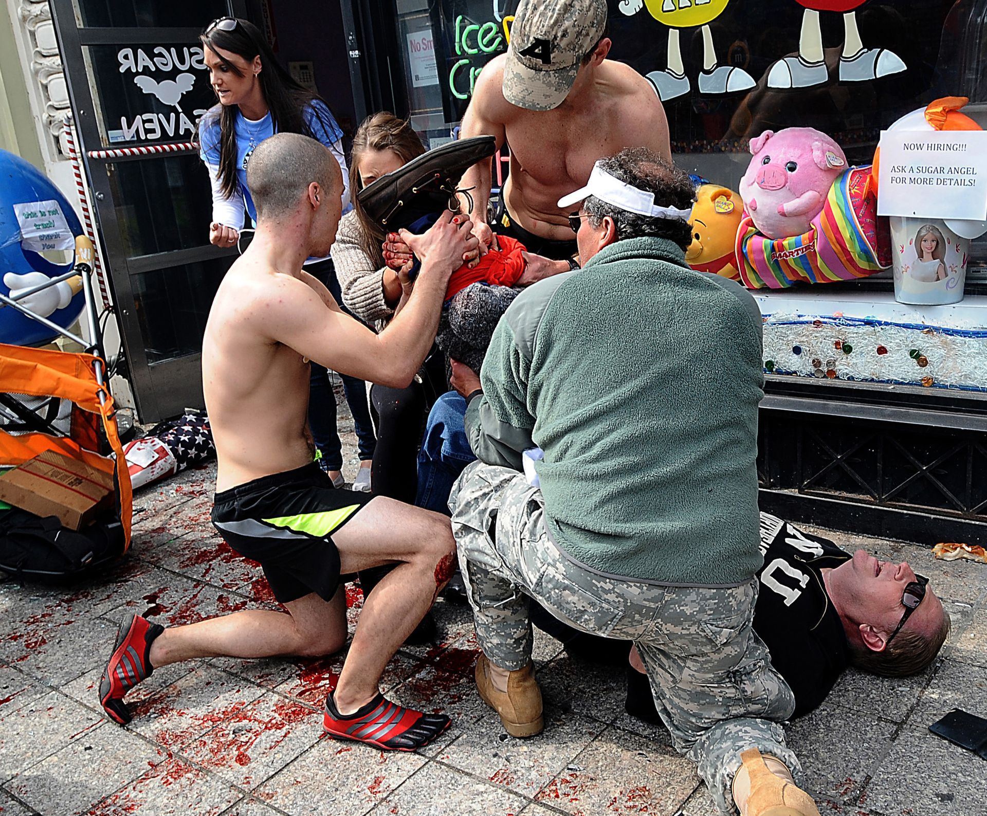 Boston marathon competitor Robert Wheeler kneeling at left, helps a man injured after the bombings at the Boston Marathon finish line, April 15, 2013.