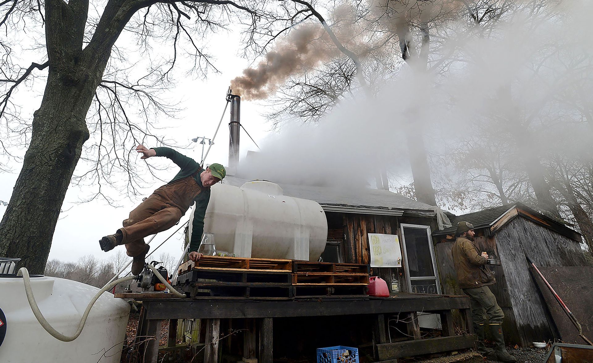 Rusty Varrell, 19, of Holliston, climbs down as steam from the evaporator and smoke from a wood fire pour from the Natick Community Organic Farm maple sugar shack, March 27, 2015.