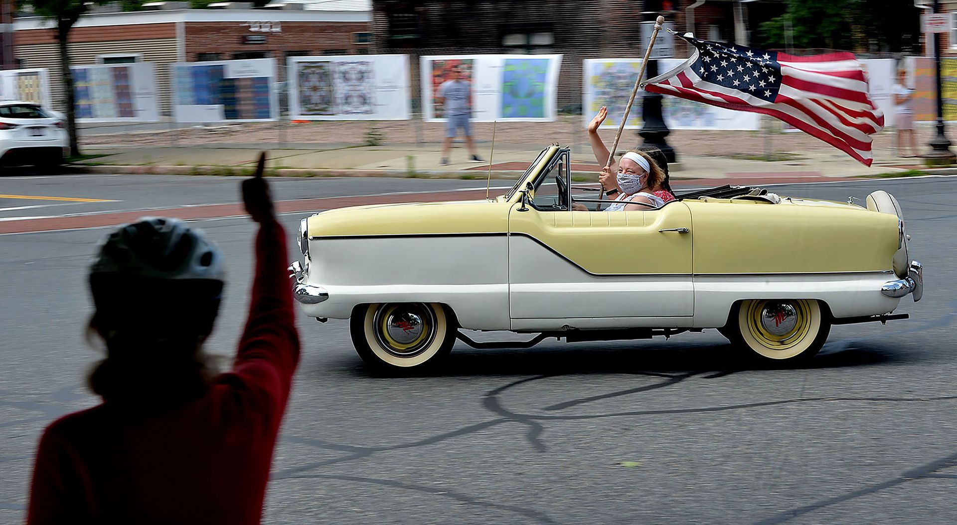 A spectator gives the thumbs up as Beth Byrne and her 1959 Nash Metropolitan speed through Natick Center during a Fourth of July classic car tour on Saturday, July 4, 2020.