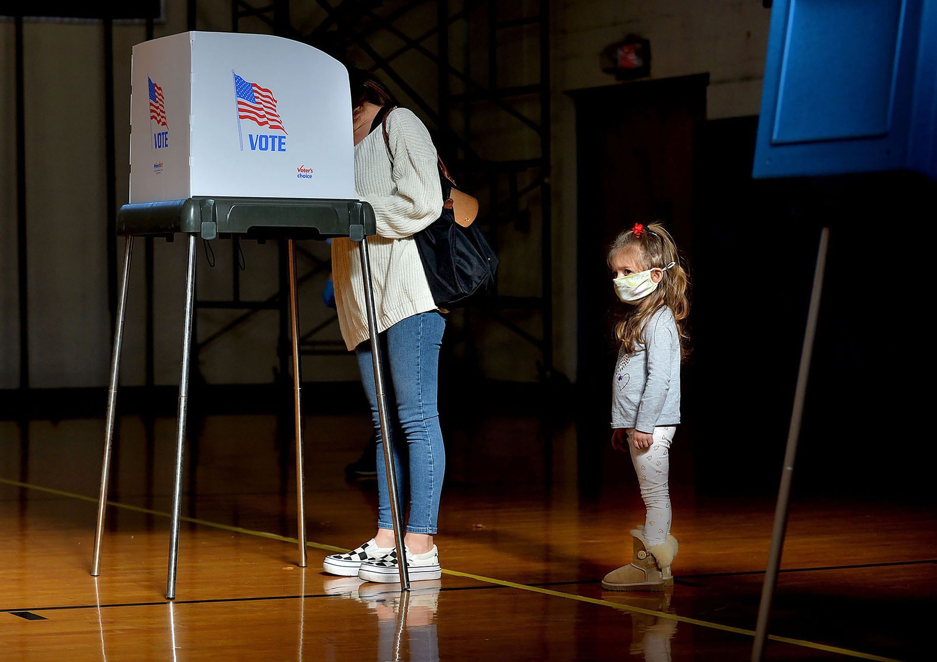 Kaia Calnan, 3, is illuminated by sunlight coming in through the gym windows as her mother, Jillian Calnan, votes at Hopedale's Draper Gymnasium polling station on Election Day, Nov. 3, 2020.