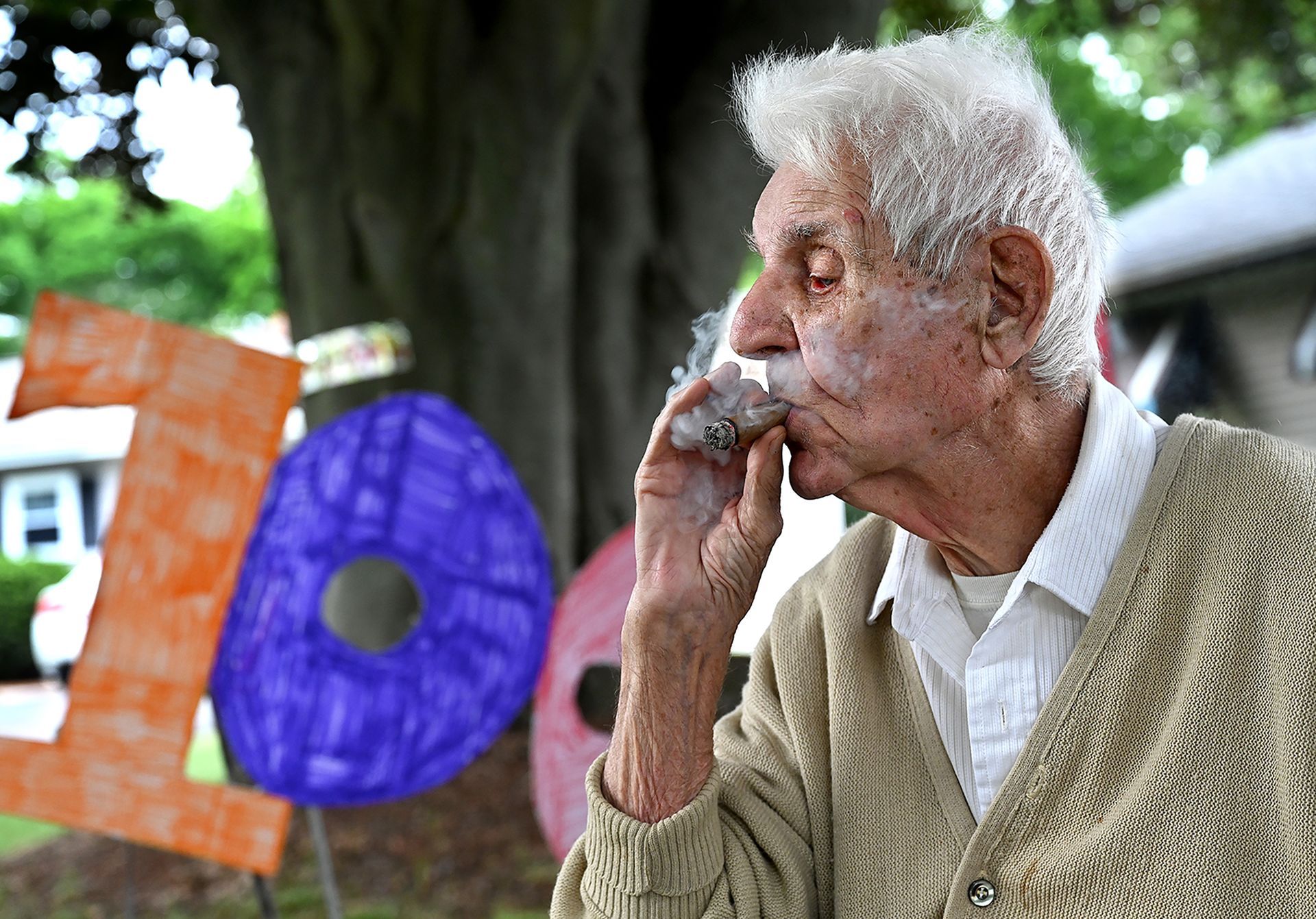 On his 100th birthday, Earl Haley of Framingham smokes a cigar as a waits for a birthday parade of antique cars, Brewster ambulances, the Framingham Fire Department and Framingham residents to arrive at his Pincusion Road home on Wednesday, June 3.