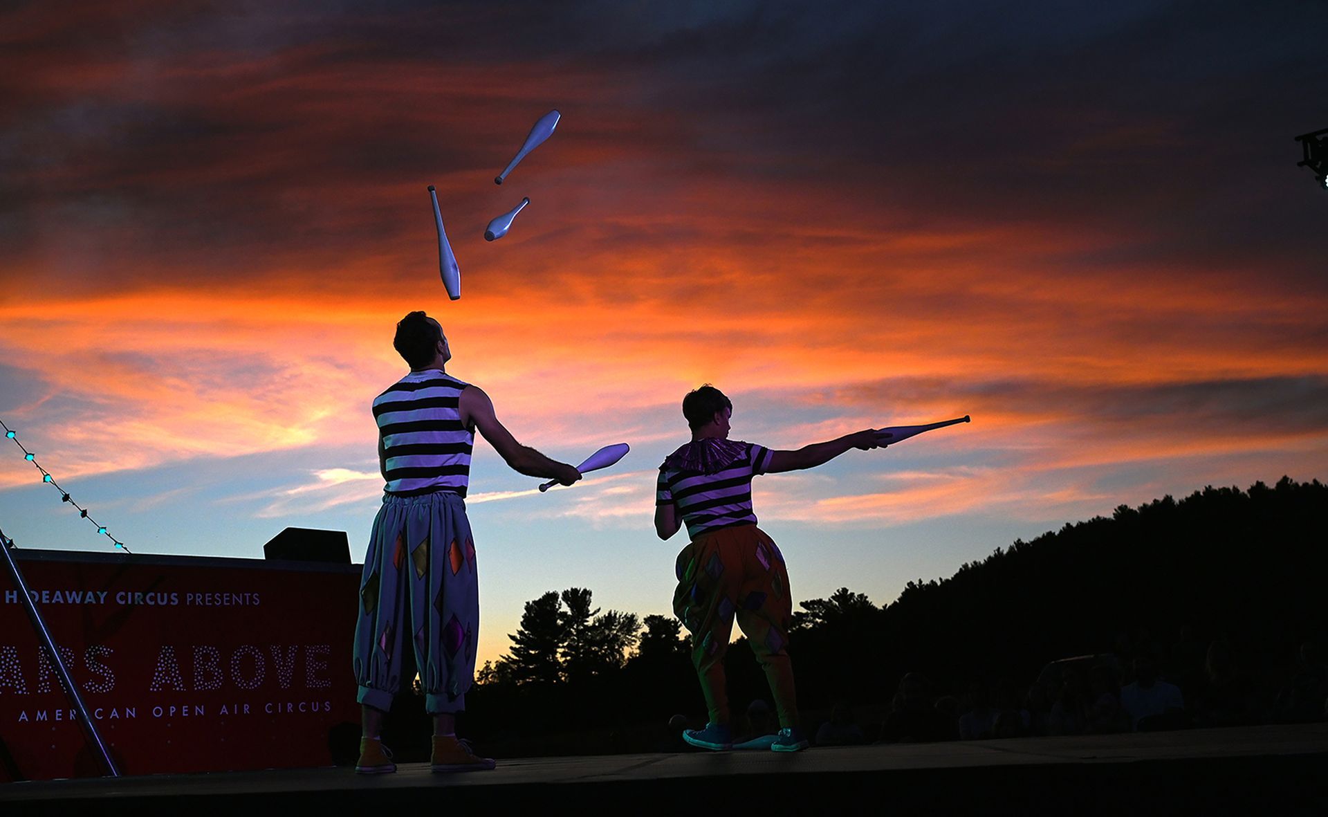 Jugglers Aaron Dewitt and Willem McGowan perform as the sun sets during the Stars Above open-air circus show at Eastleigh Farm in Framingham, Aug. 12, 2022. A troupe of ten circus artists from New York-based Hideaway Circus put on a show that is a blend of contemporary and classic circus for a rapt audience of children and adults.
