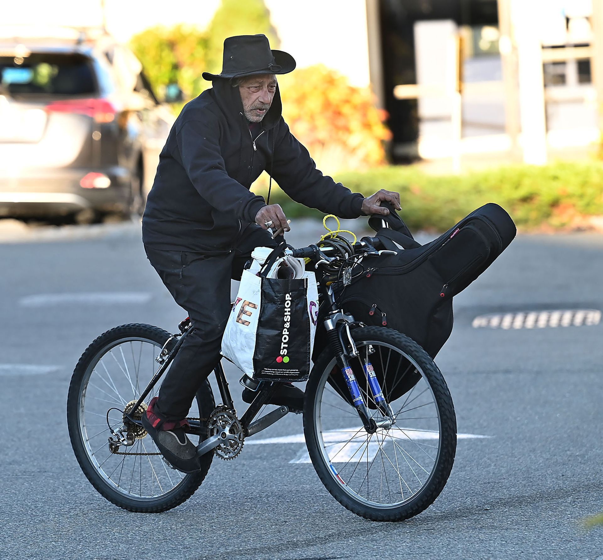 Guitar player Bobby Consoletti carries his gear a short distance from the 7-Eleven to Nathan's Jewelers in downtown Milford, where owner Nathan Sophos lets him store his guitar behind the counter, Nov. 6, 2021.