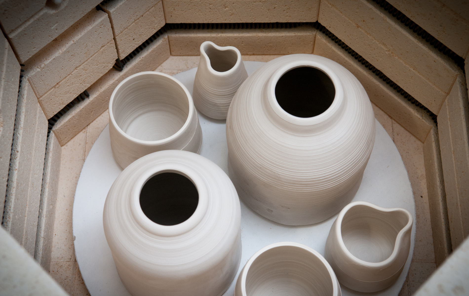 A group of white vases are sitting inside of a kiln