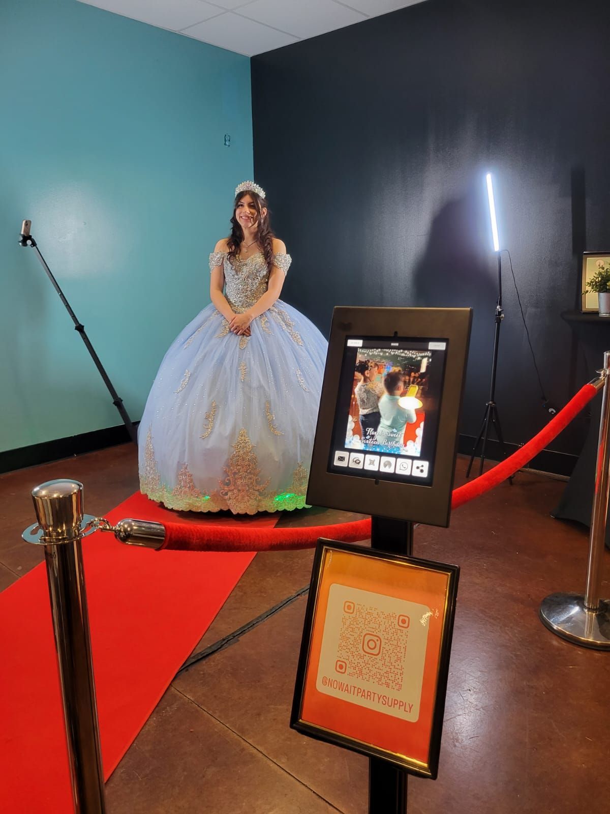 A woman in a white dress is standing on a red carpet in front of a photo booth.