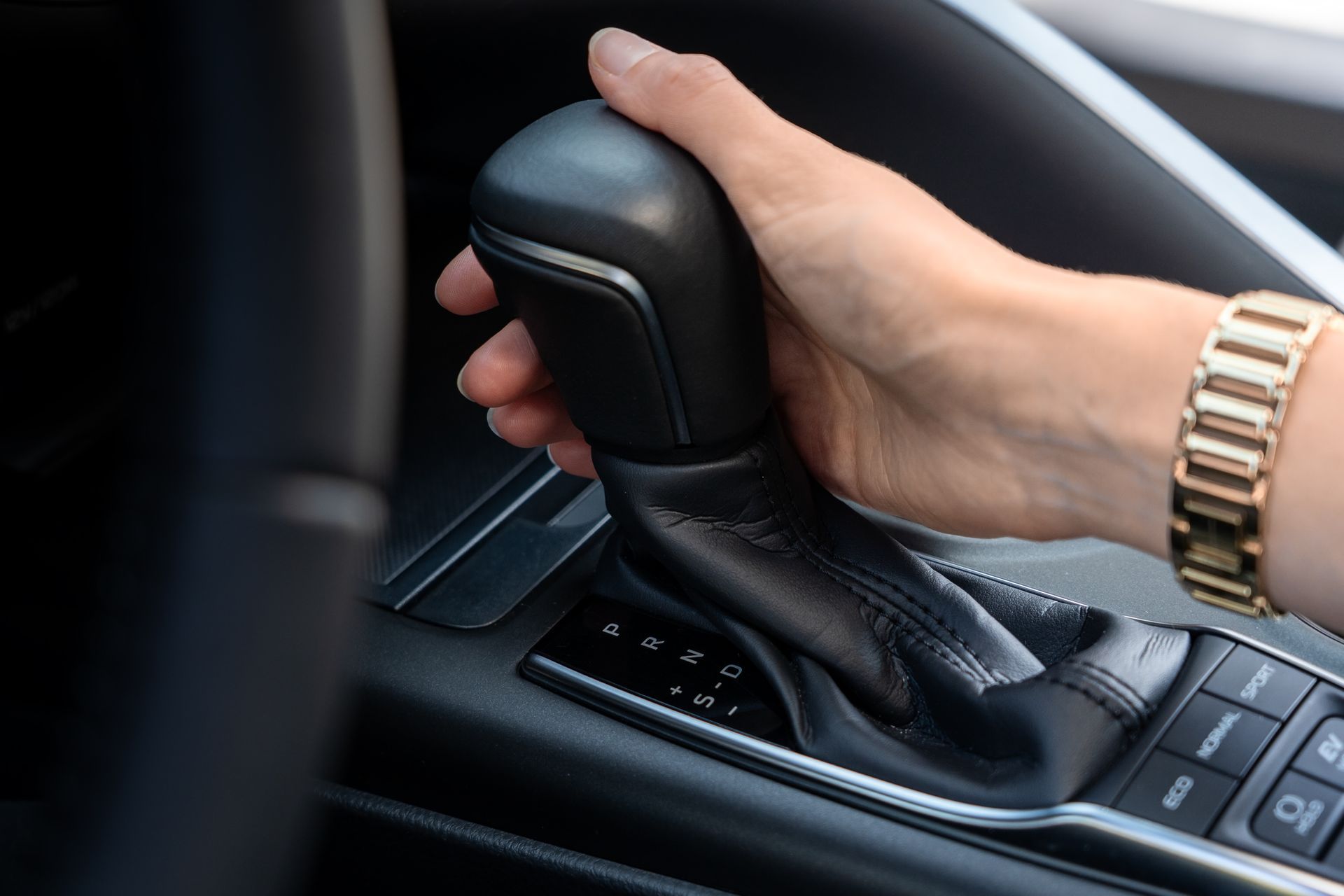 Woman’s hand on auto gear shift showing PRND and drive modes in modern car interior.