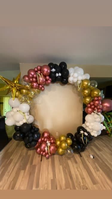 Balloon wreath with black, gold, white, and rose-colored balloons encircling a beige backdrop.