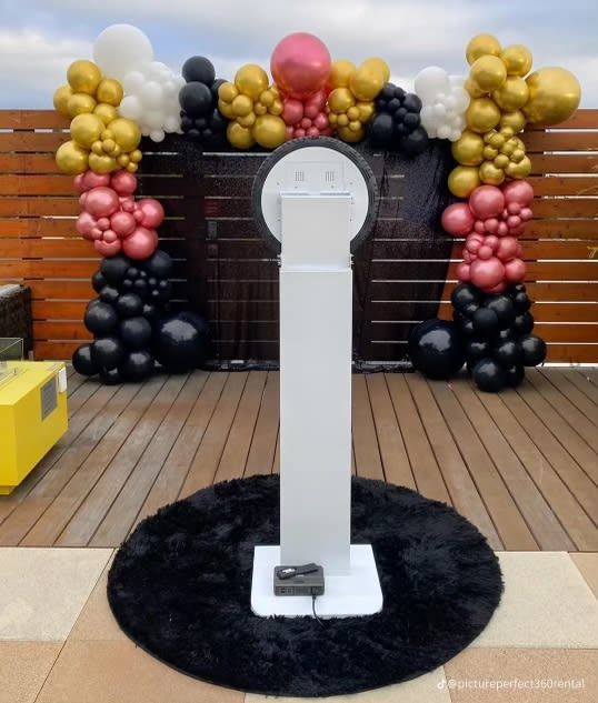Photo booth on a black rug with a balloon arch backdrop, outdoors.