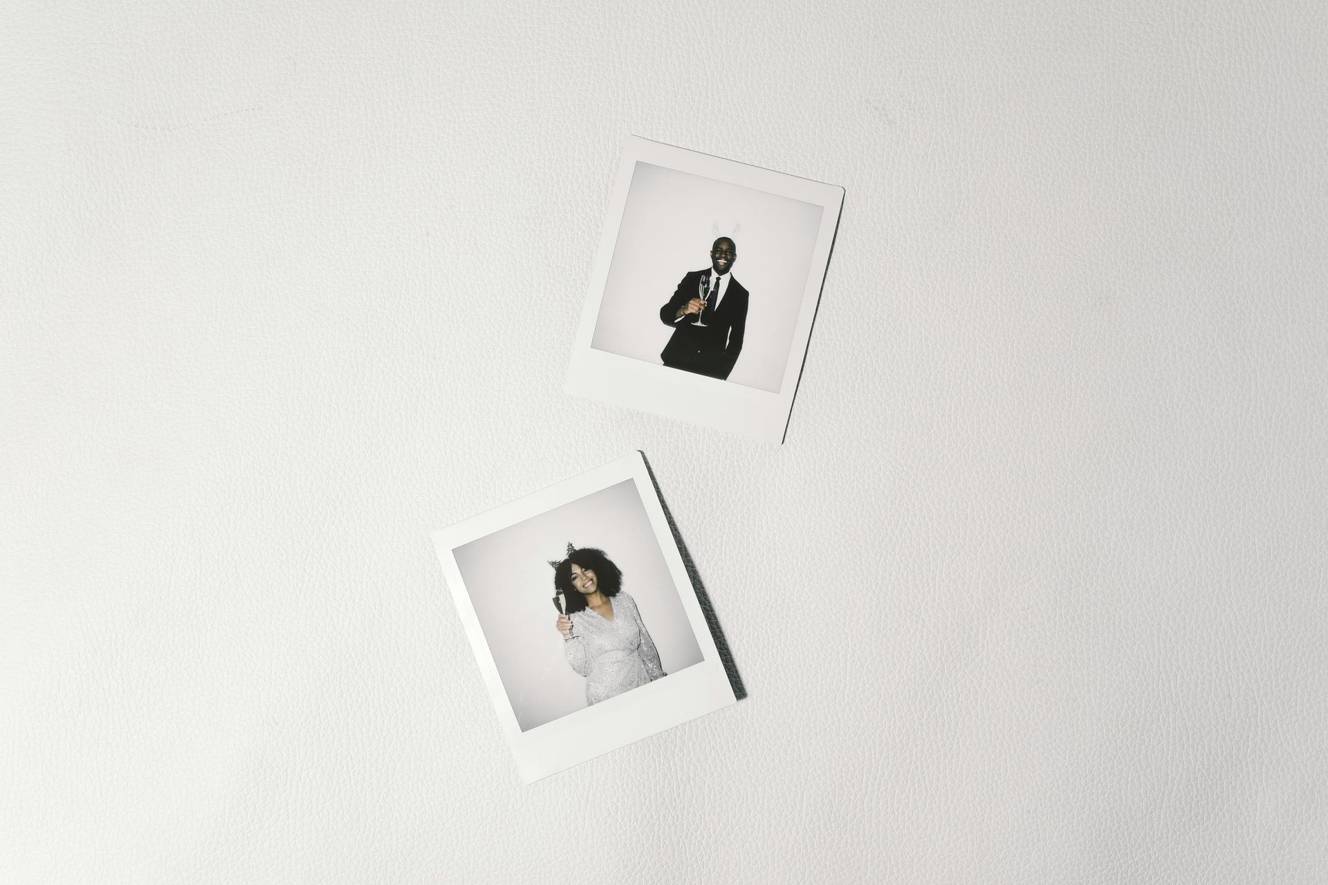 Two polaroid photos pinned to a white wall: one showing a person in a suit, the other a person wearing cat ears.