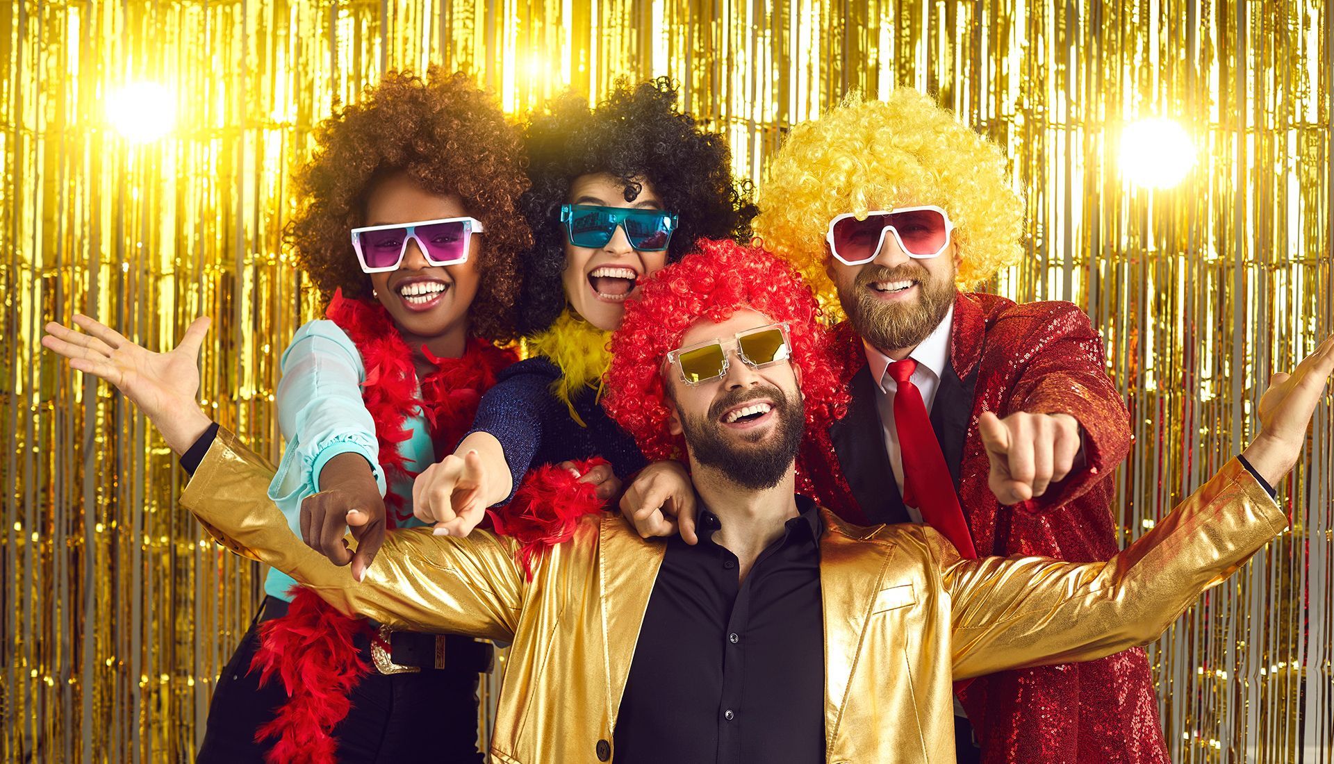 People in wigs and sunglasses pose for a photo in front of a gold curtain.