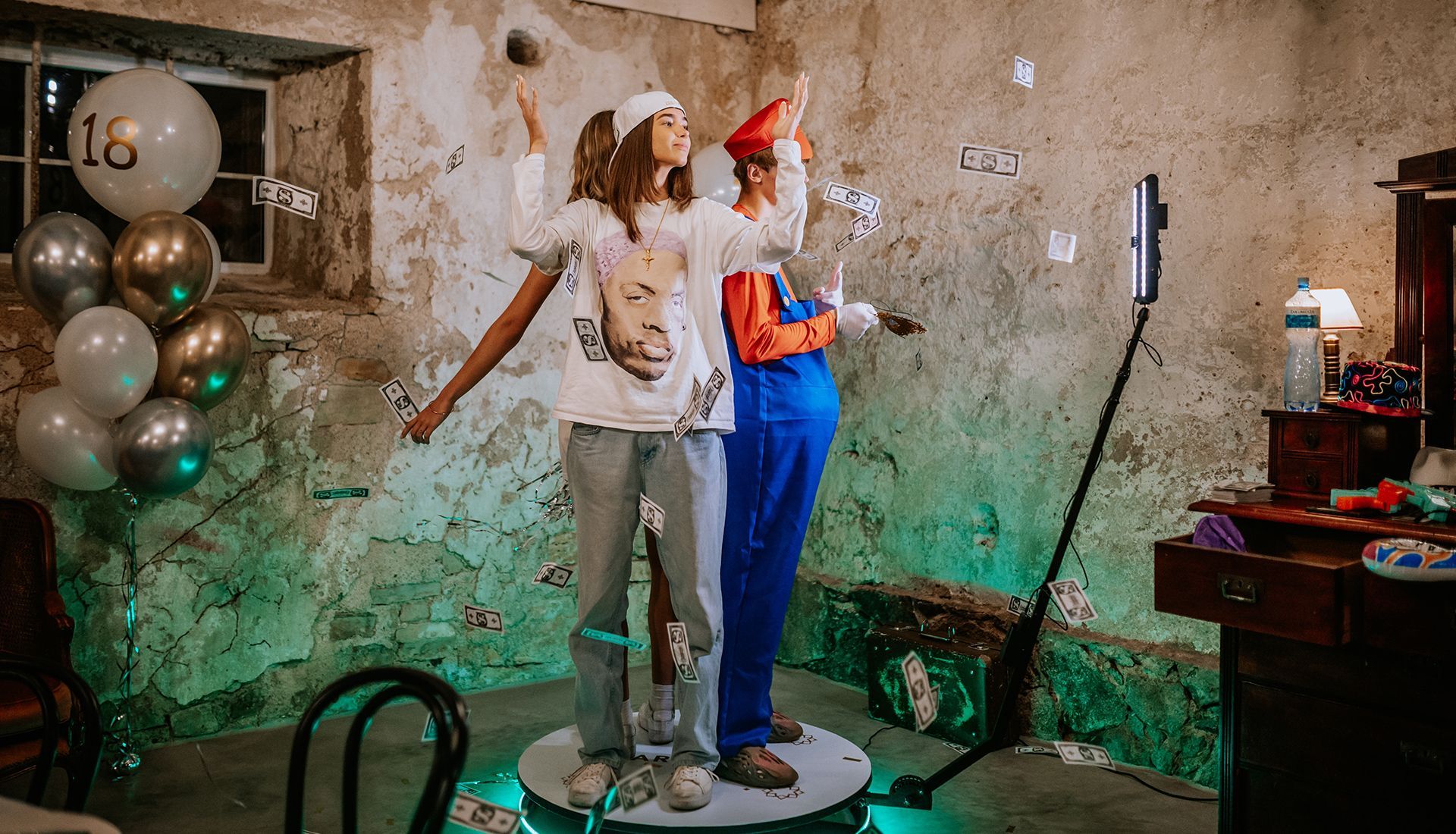Two people on a rotating platform, one dressed as Mario, the other with a graphic tee, confetti around them.