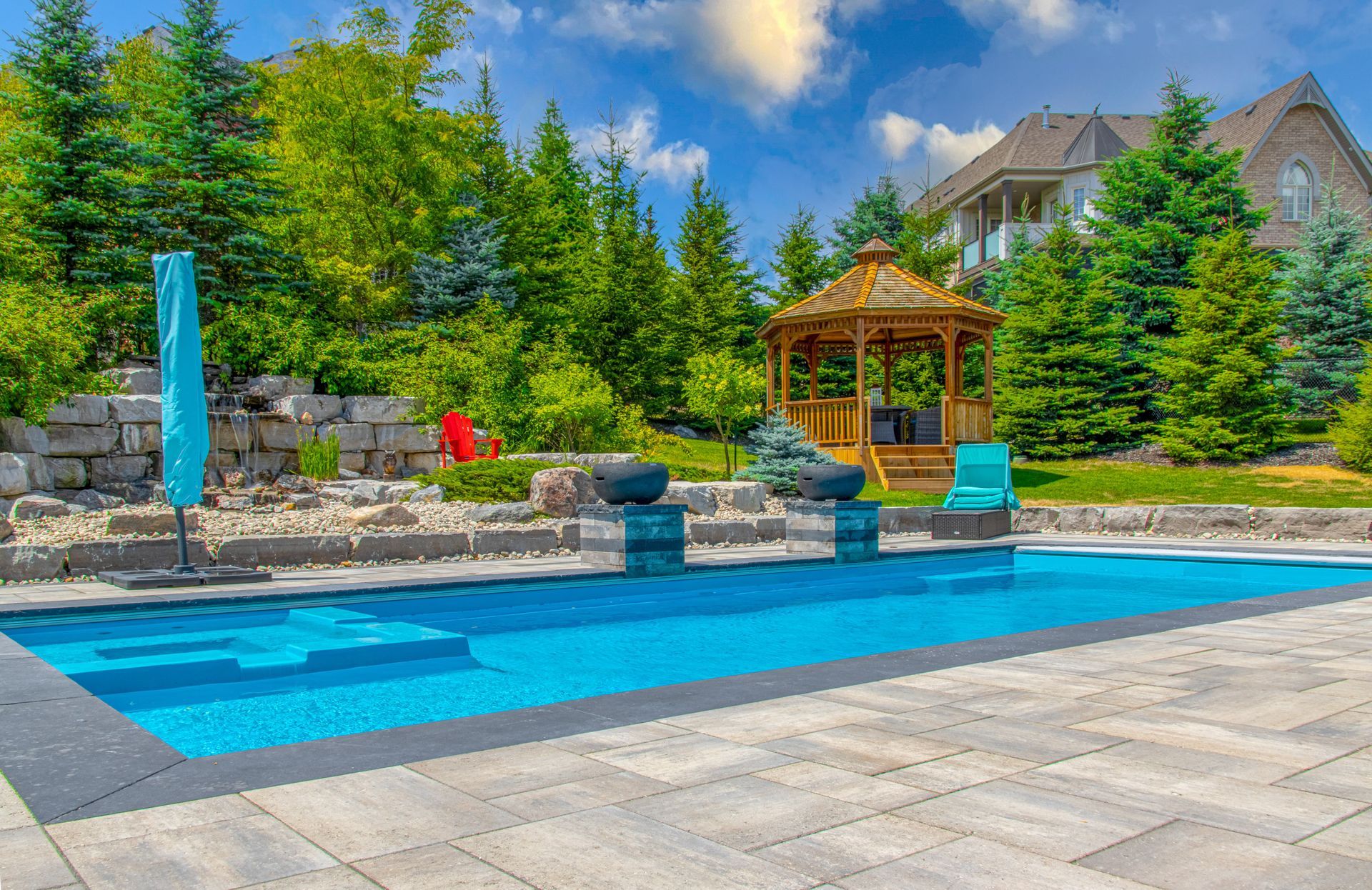 A large swimming pool is surrounded by trees and a gazebo.