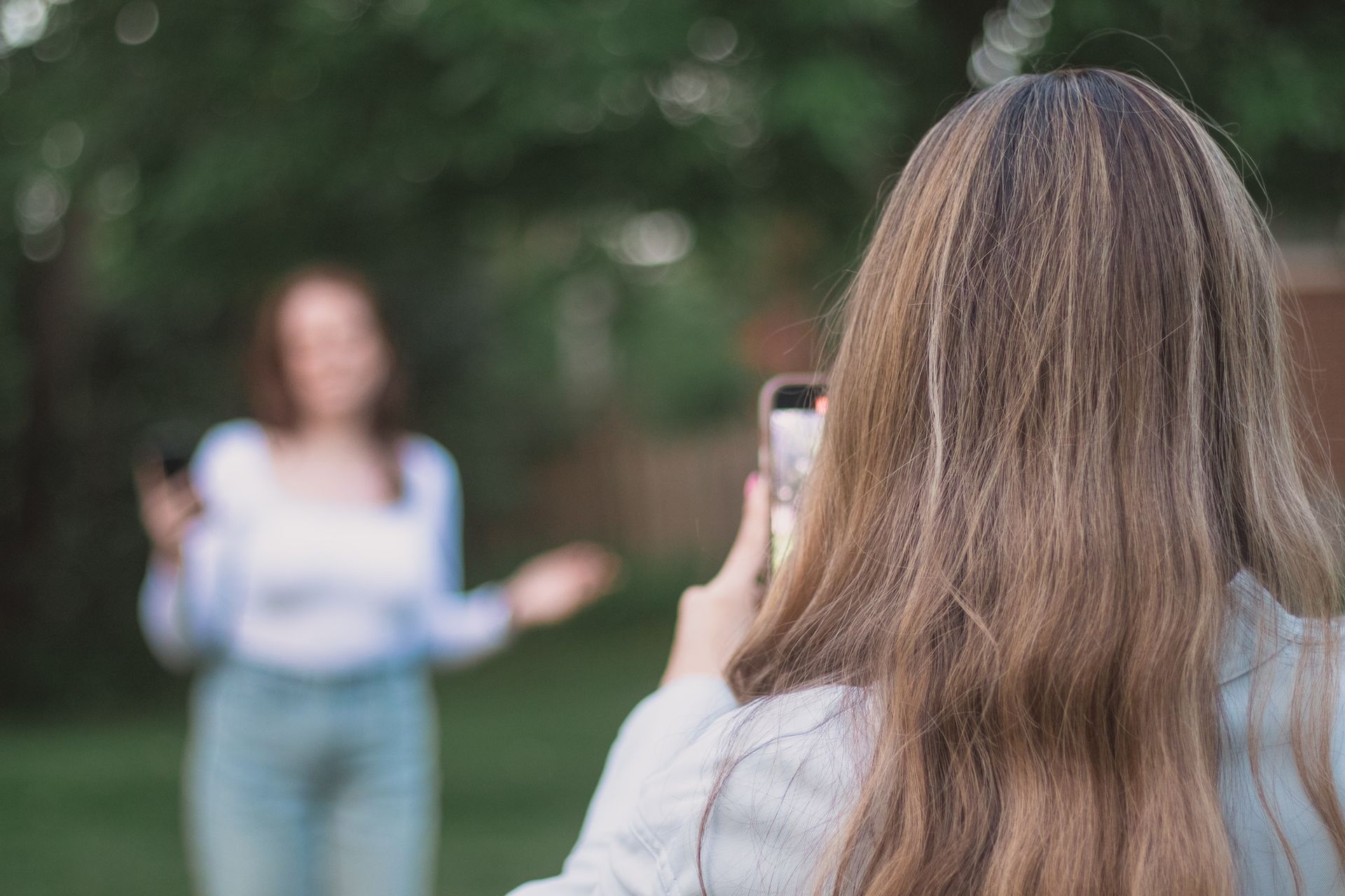 A woman is taking a picture of another woman with her cell phone.