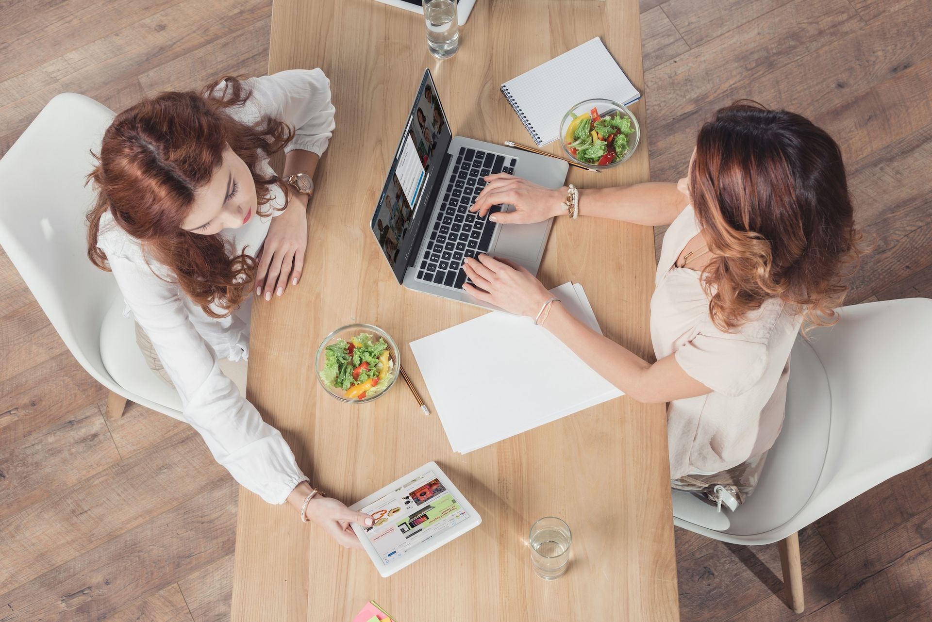 Two women are sitting at a table using laptops.