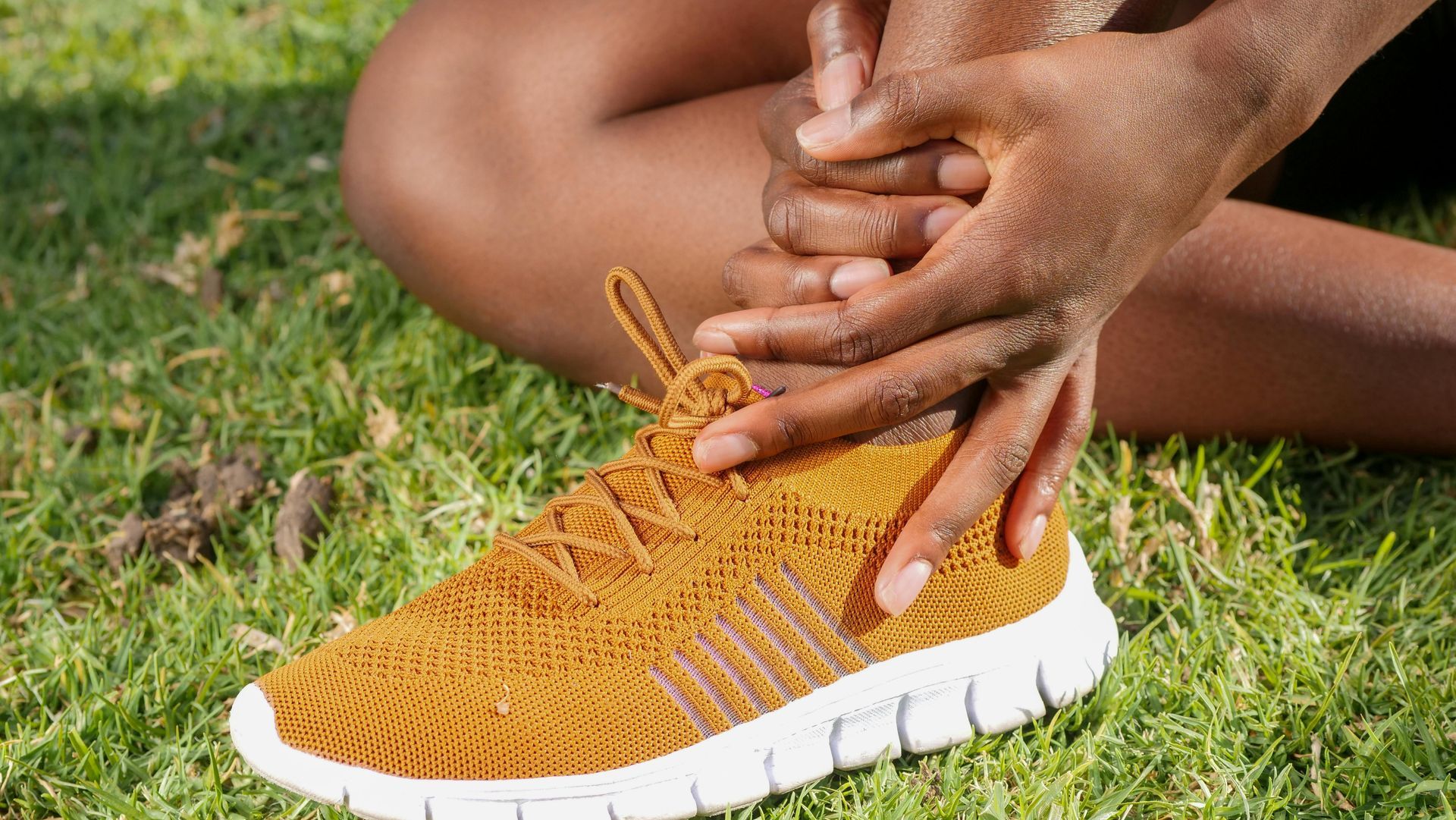 A person is sitting on the grass with their hands on their ankles.