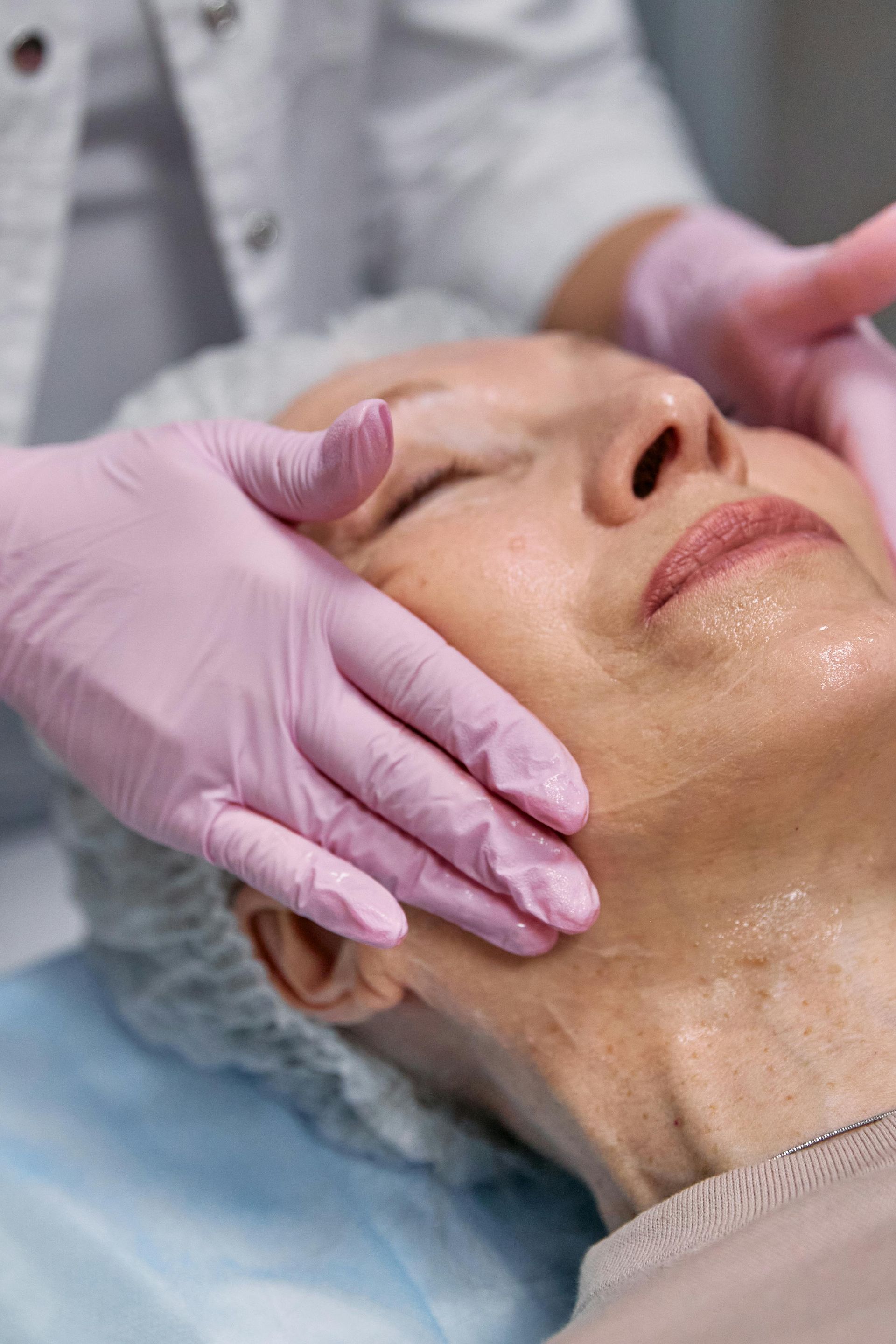 Unas manos enguantadas masajean suavemente el rostro de una mujer en un tratamiento de spa.