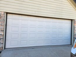 A white garage door is sitting in front of a brick house.