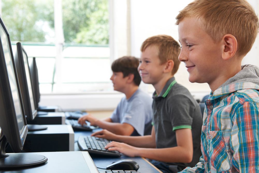 Tre ragazzi sorridenti, che scrivono al computer in un'aula ben illuminata.