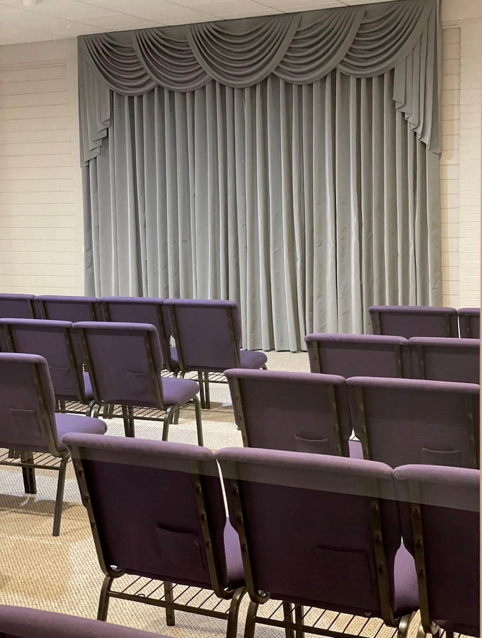 The inside of a church with rows of wooden benches and stained glass windows.