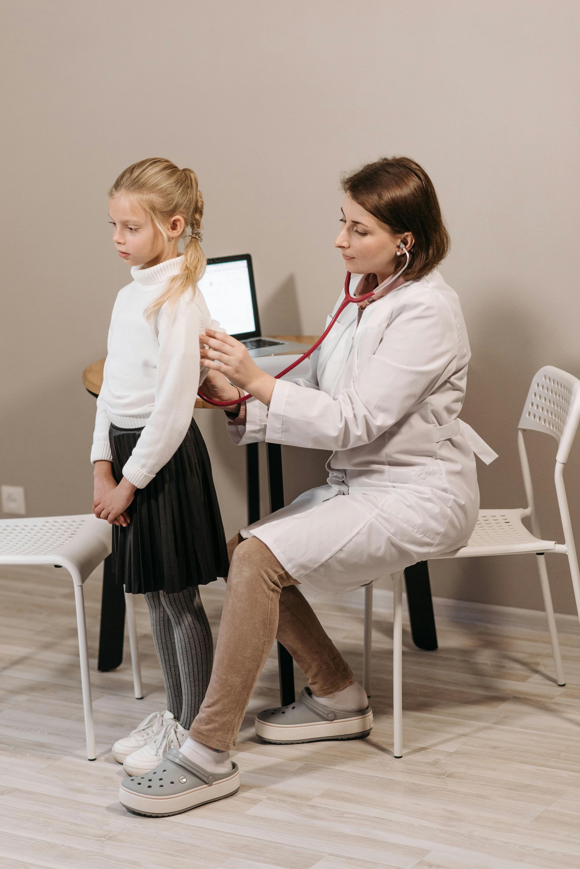 A woman is standing next to a little girl sitting on a table in a doctor 's office.