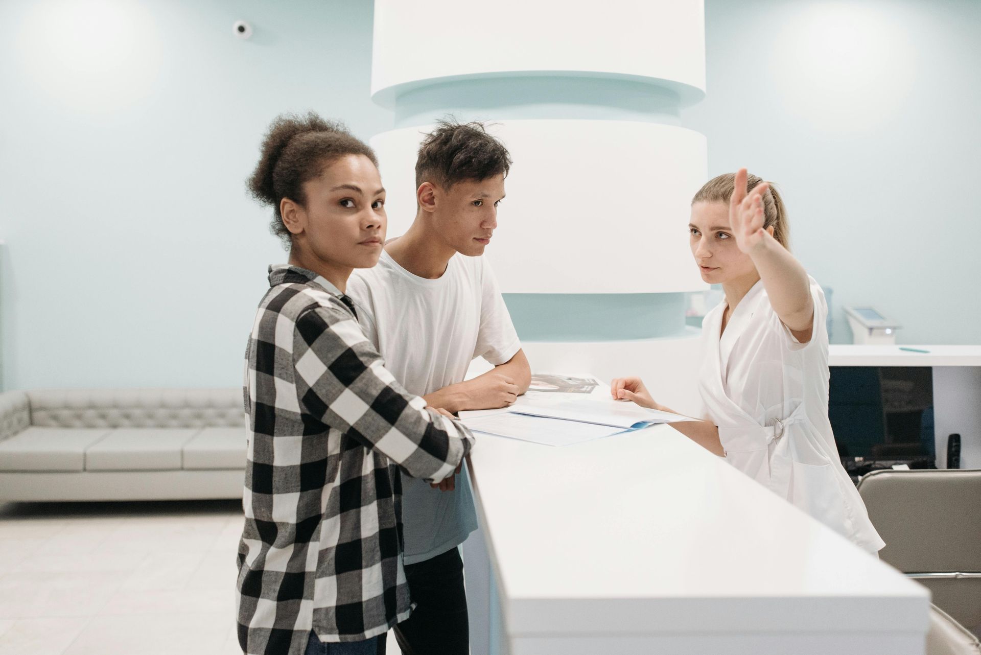 Two young adults speaking to medical professional at desk.