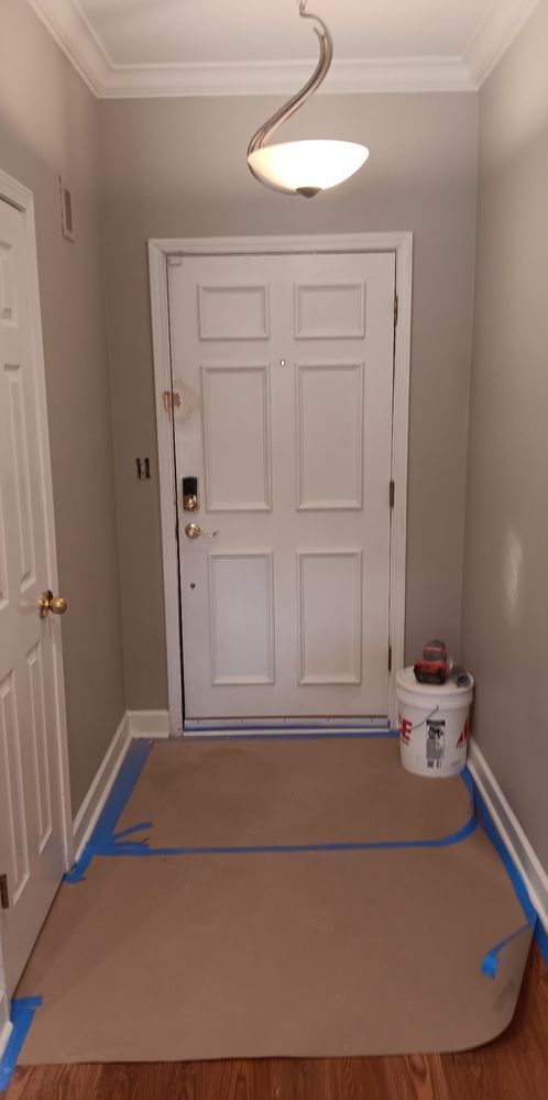 A hallway with a white door and a bucket of paint on the floor.