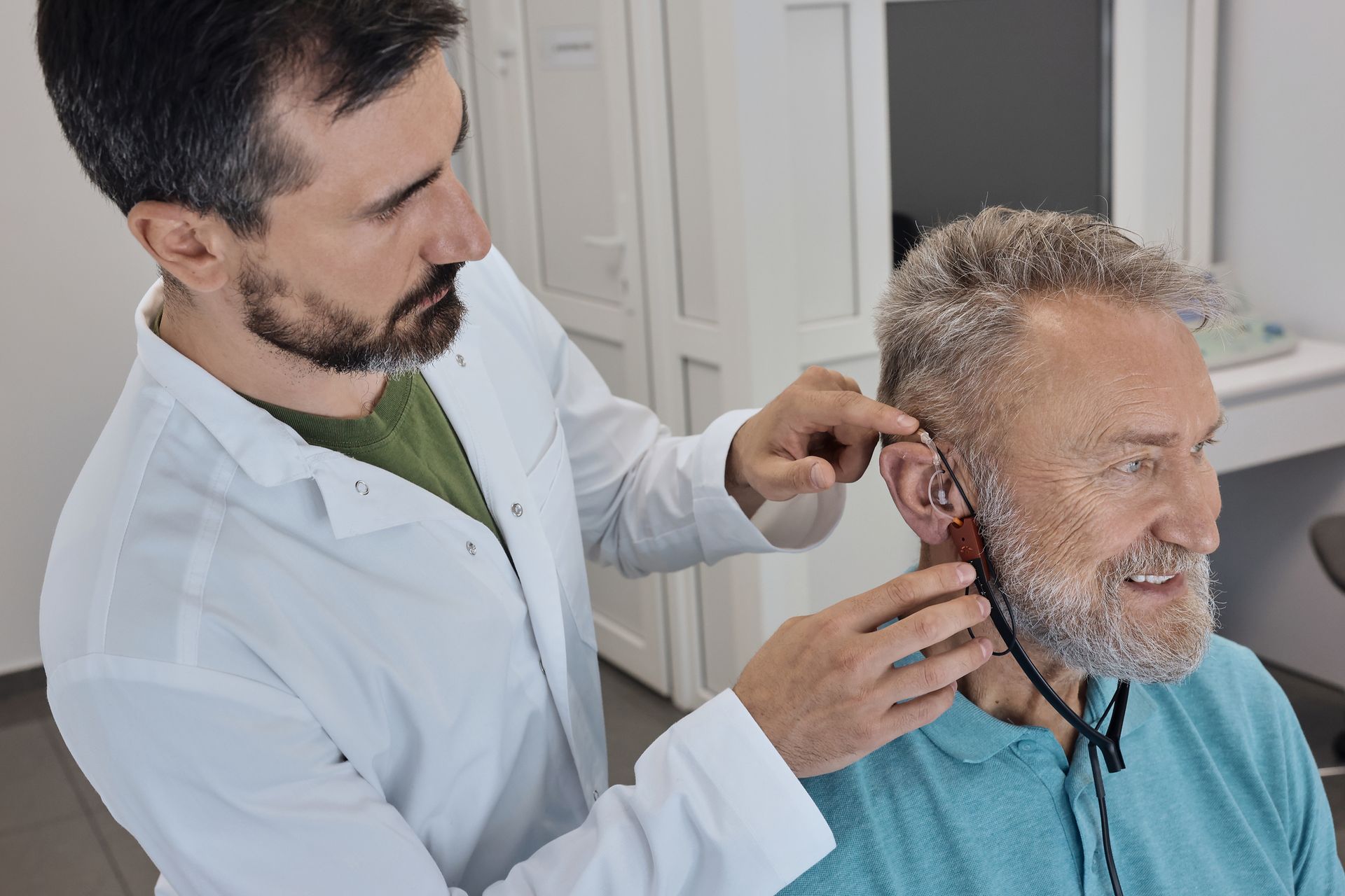 Audiologist testing and installing hearing aid on a senior patient. Audiologist testing and installing hearing aid on a senior patient.