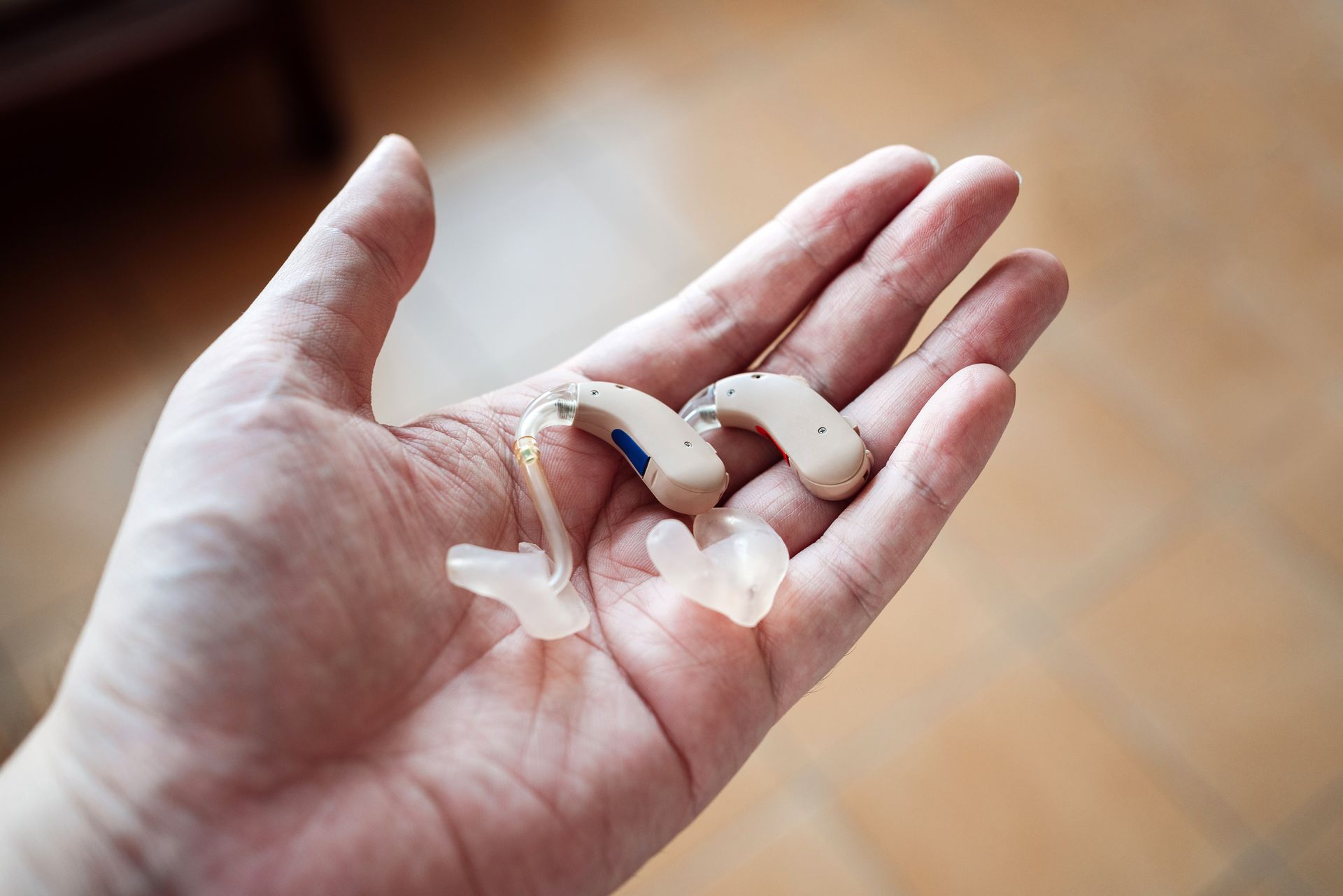 Closeup of hearing aid repair, person holds two hearing aids in open palm on warm background.