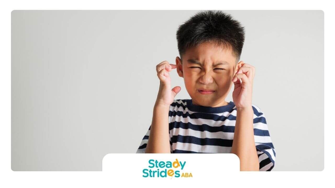 Young boy with autism covering his ears and squinting in discomfort.