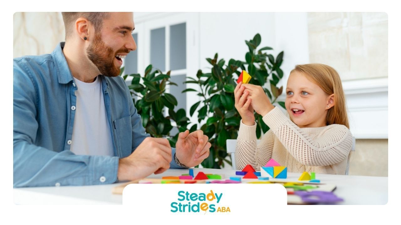 A BCBA and a little girl are playing with blocks at a table.