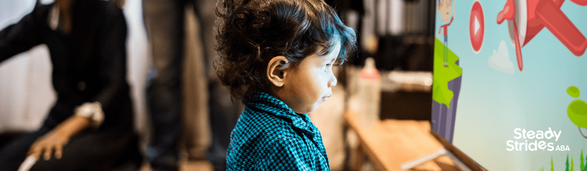 Autistic boy watching educational content on a TV screen while holding a tablet, with therapists.