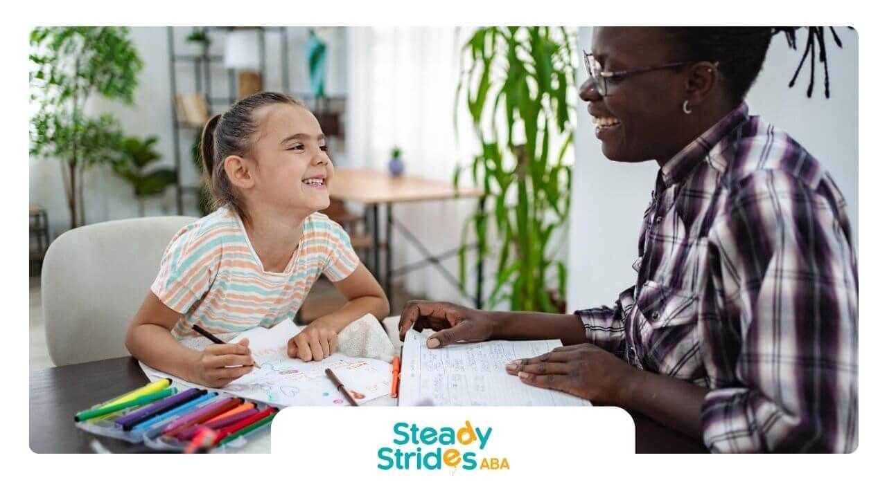 Young girl with autism laughing while working on homework with an ABA therapist.