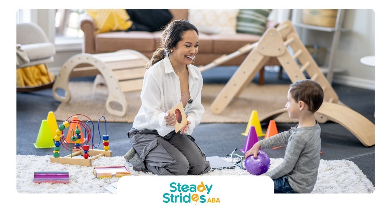 Woman interacting with a child, surrounded by play equipment, smiling in an indoor setting.