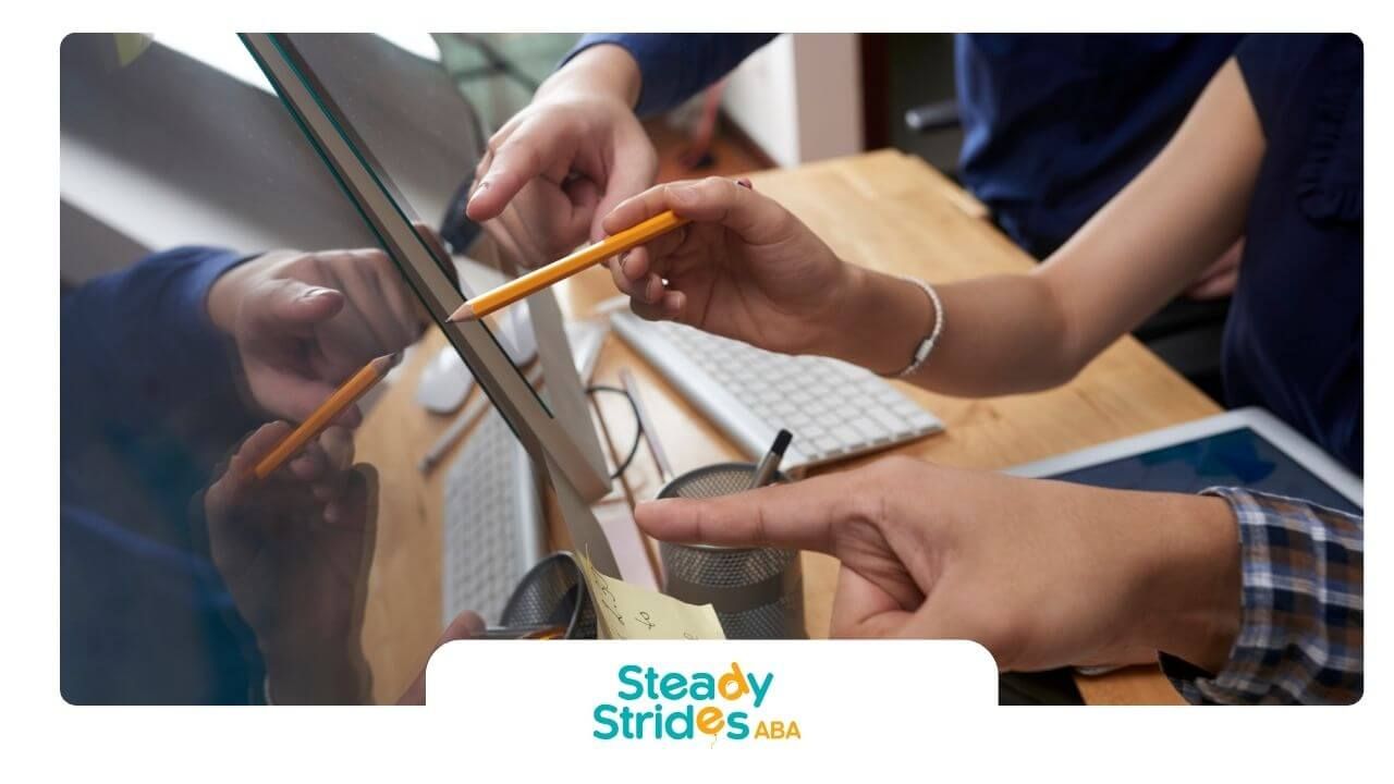 Two therapists pointing at computer monitor and tablet screen while discussing notes at office desk